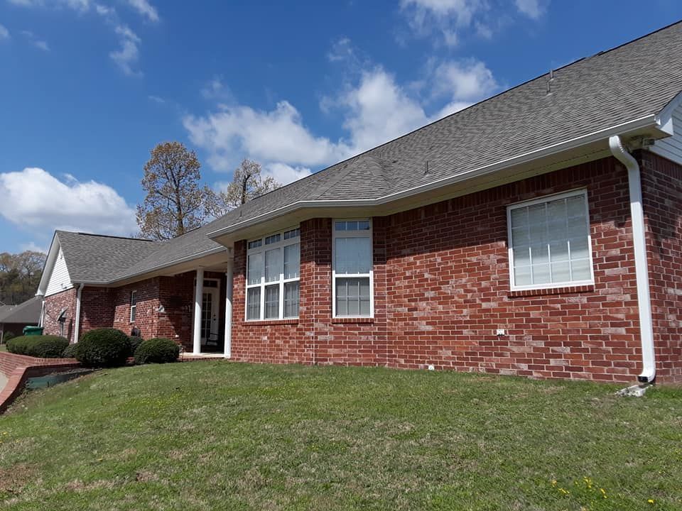 A red brick house with a gray roof and white trim is sitting on top of a lush green lawn.