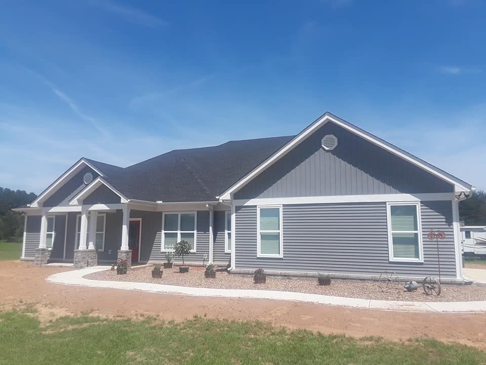 A large gray house with a black roof is sitting on top of a lush green field.
