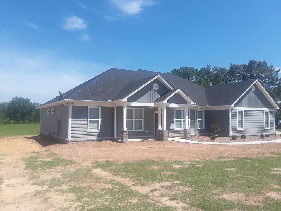 A large gray house with a black roof is sitting on top of a dirt field.