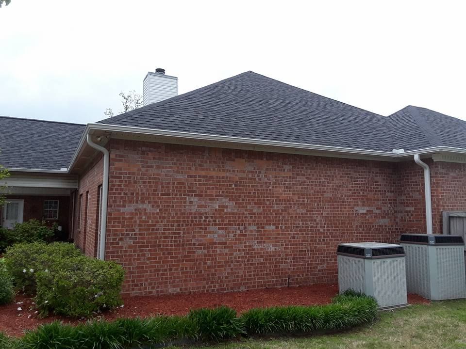 A brick house with a gray roof and two air conditioners in the backyard.