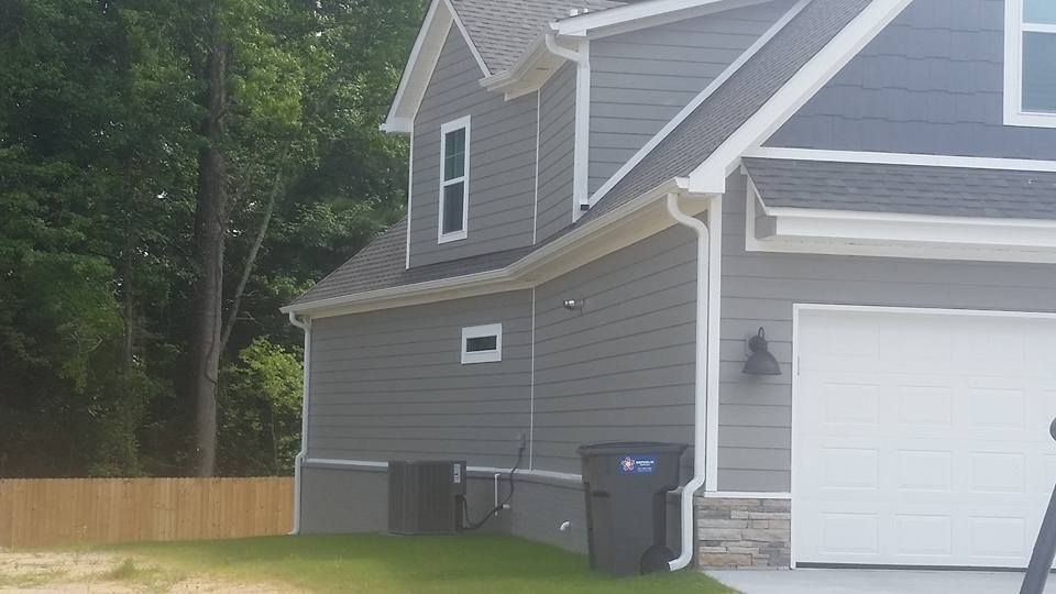 A gray house with a white garage door and two trash cans in front of it.