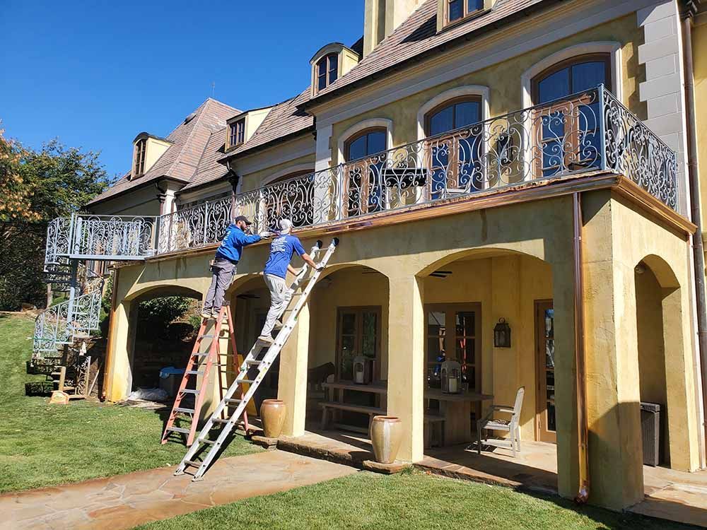 Two men are painting a balcony on the side of a house.