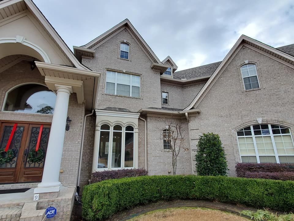 A large brick house with a lot of windows and a hedge in front of it.