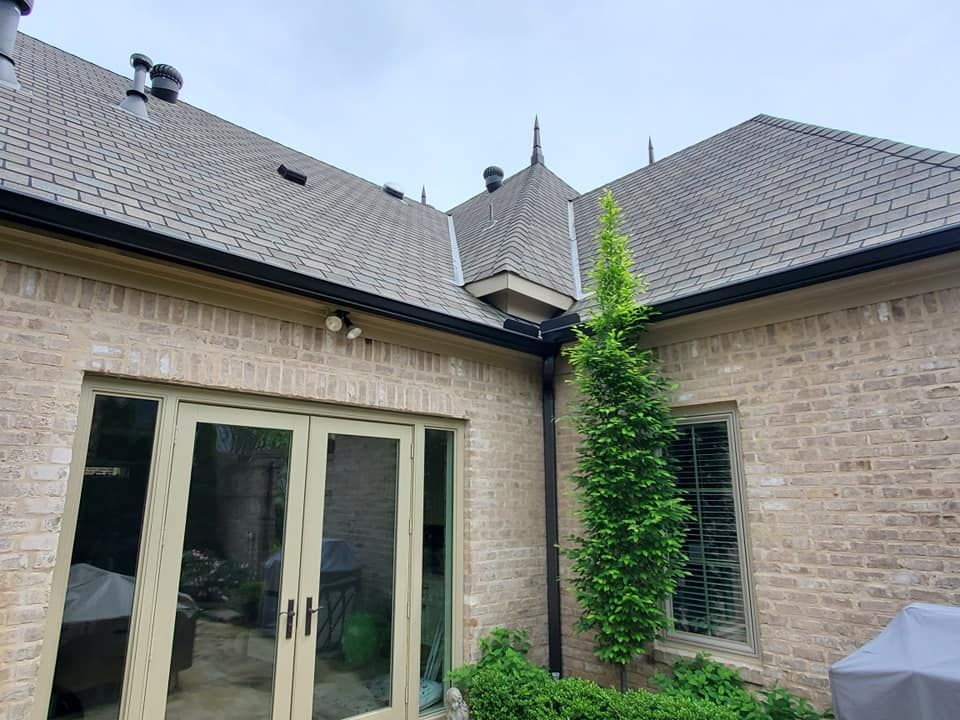 A brick house with a gray roof and a grill in the backyard.