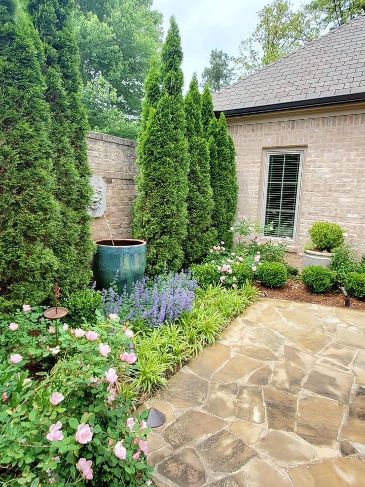 A stone walkway leading to a brick house surrounded by trees and flowers.