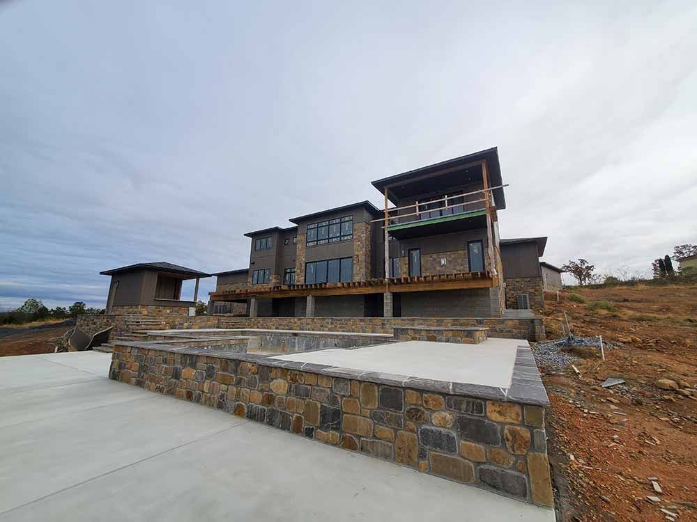 A large house is sitting on top of a hill next to a stone wall.