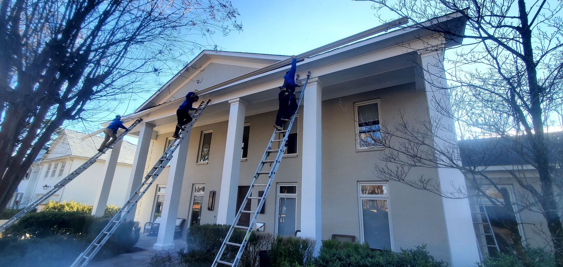 A man is standing on a ladder in front of a large white house.