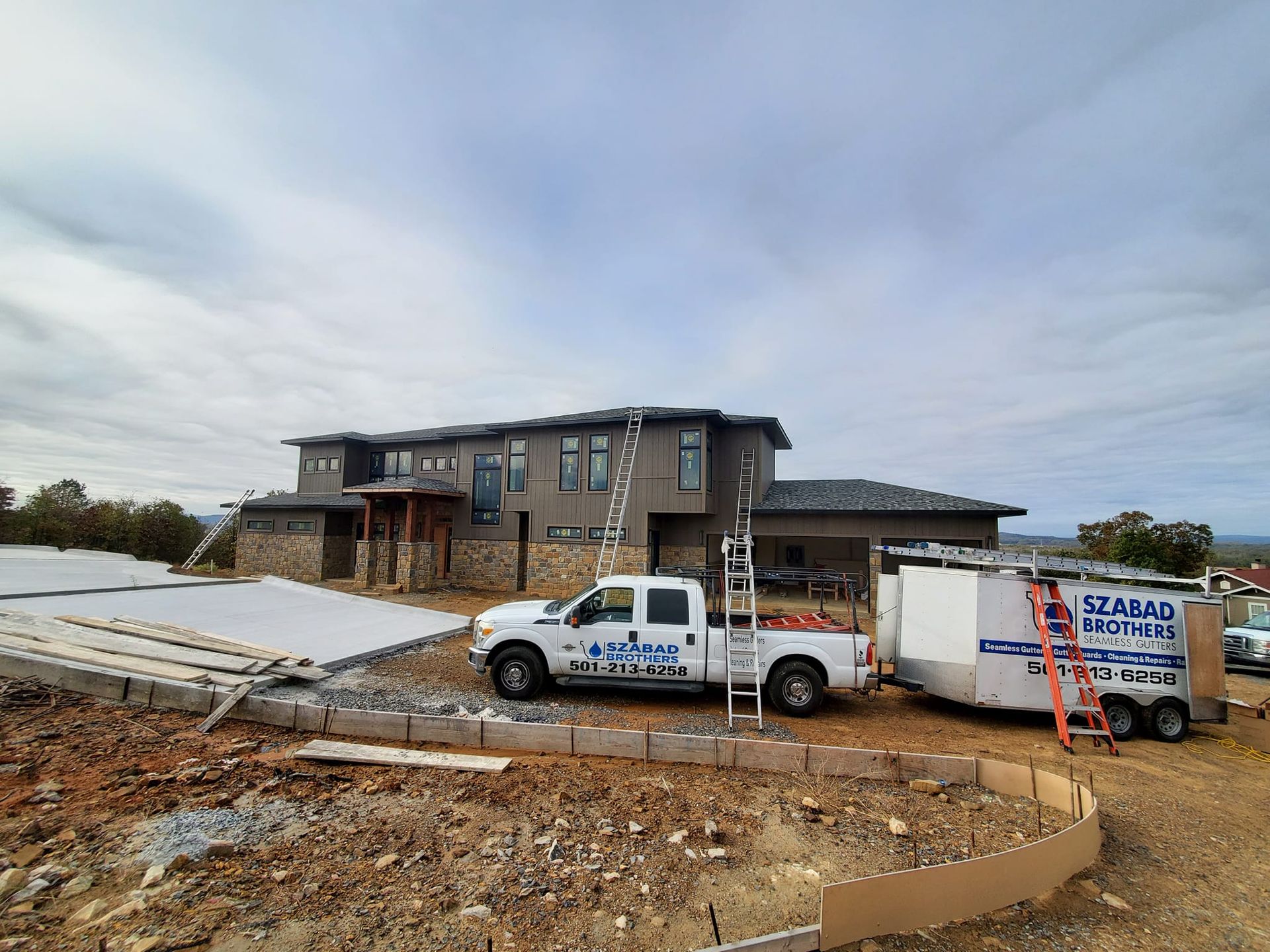 Two trucks are parked in front of a large house under construction.