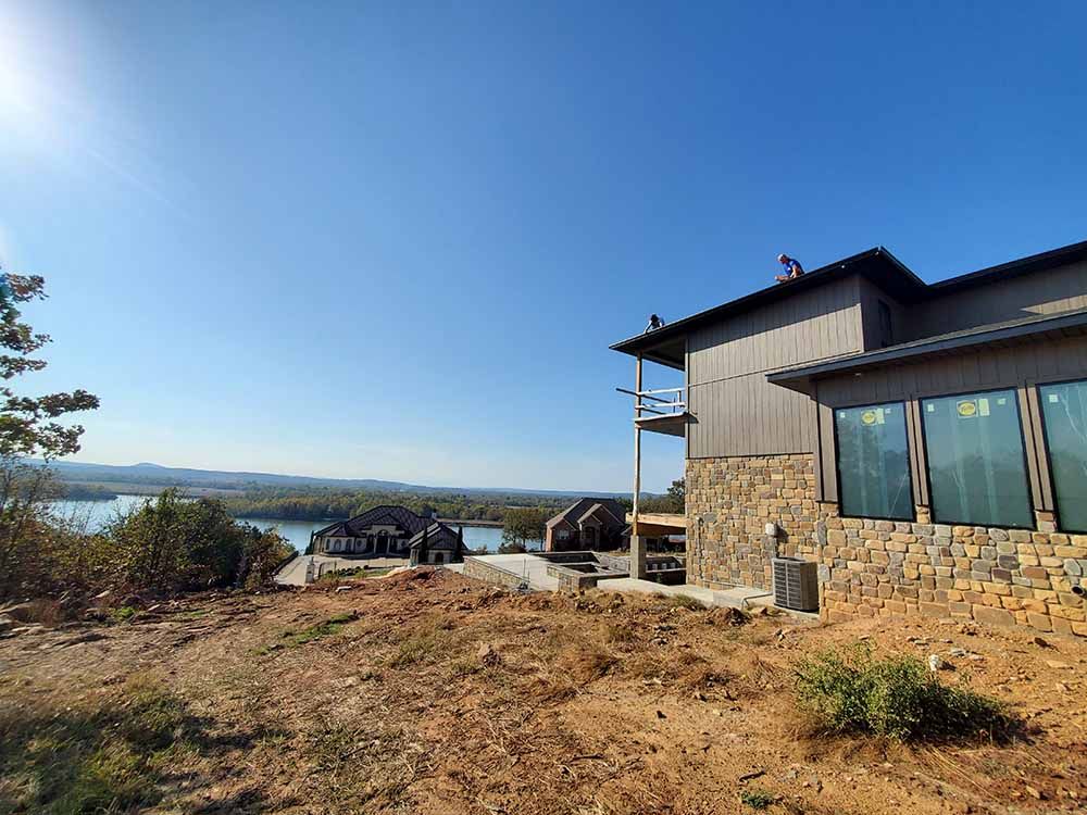 A large house is sitting on top of a hill overlooking a lake.