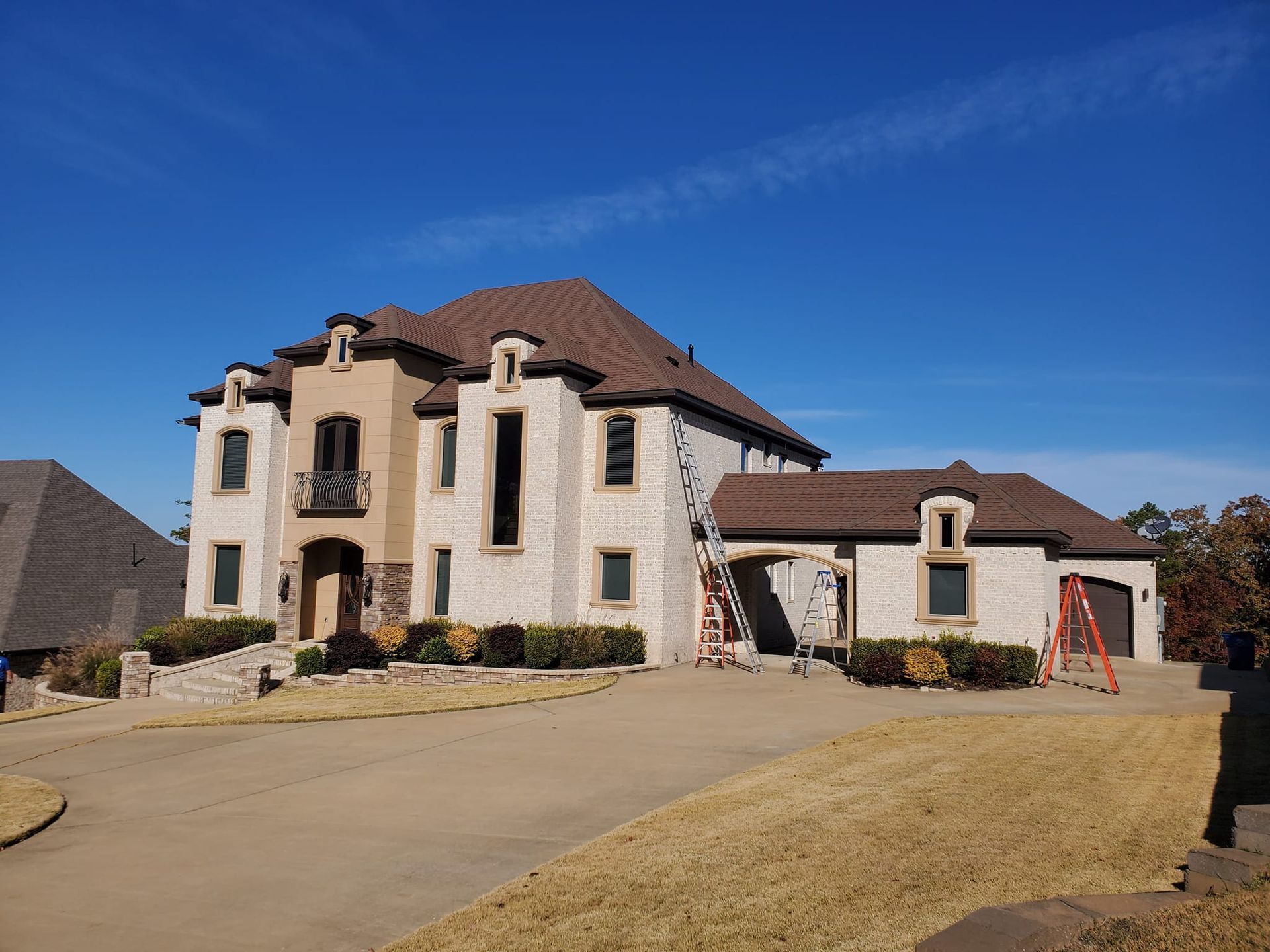 A large white house with a brown roof is being painted.