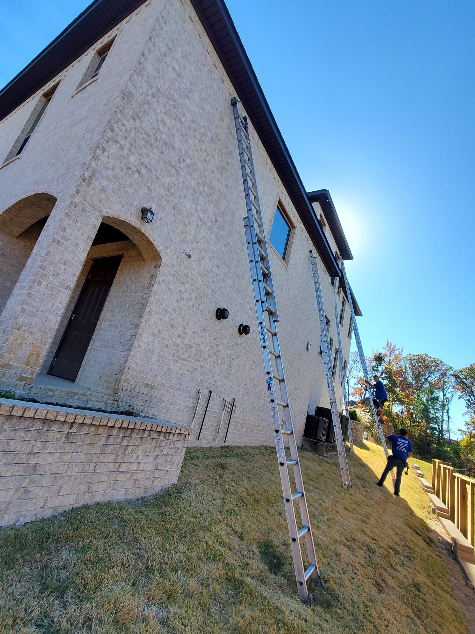 A man is standing on a ladder in front of a large house.