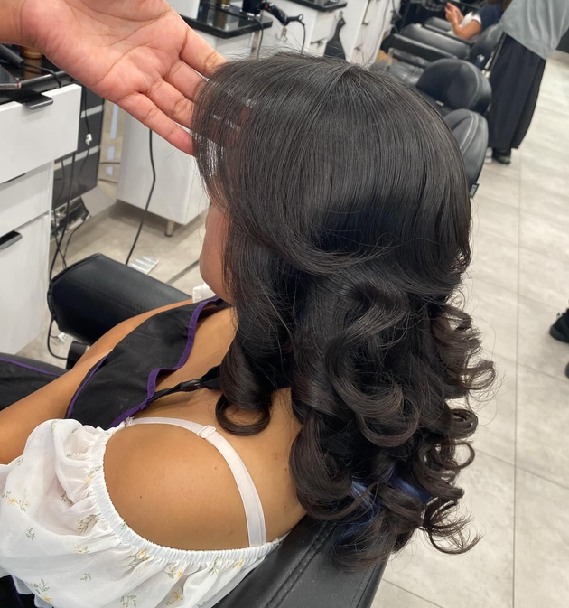 Woman with curled dark hair seated in a salon chair during a hairstyling service