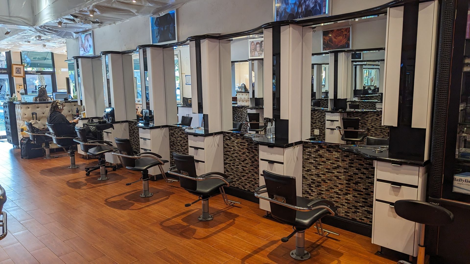 Empty salon with styling chairs and mirrors along a wooden floor.