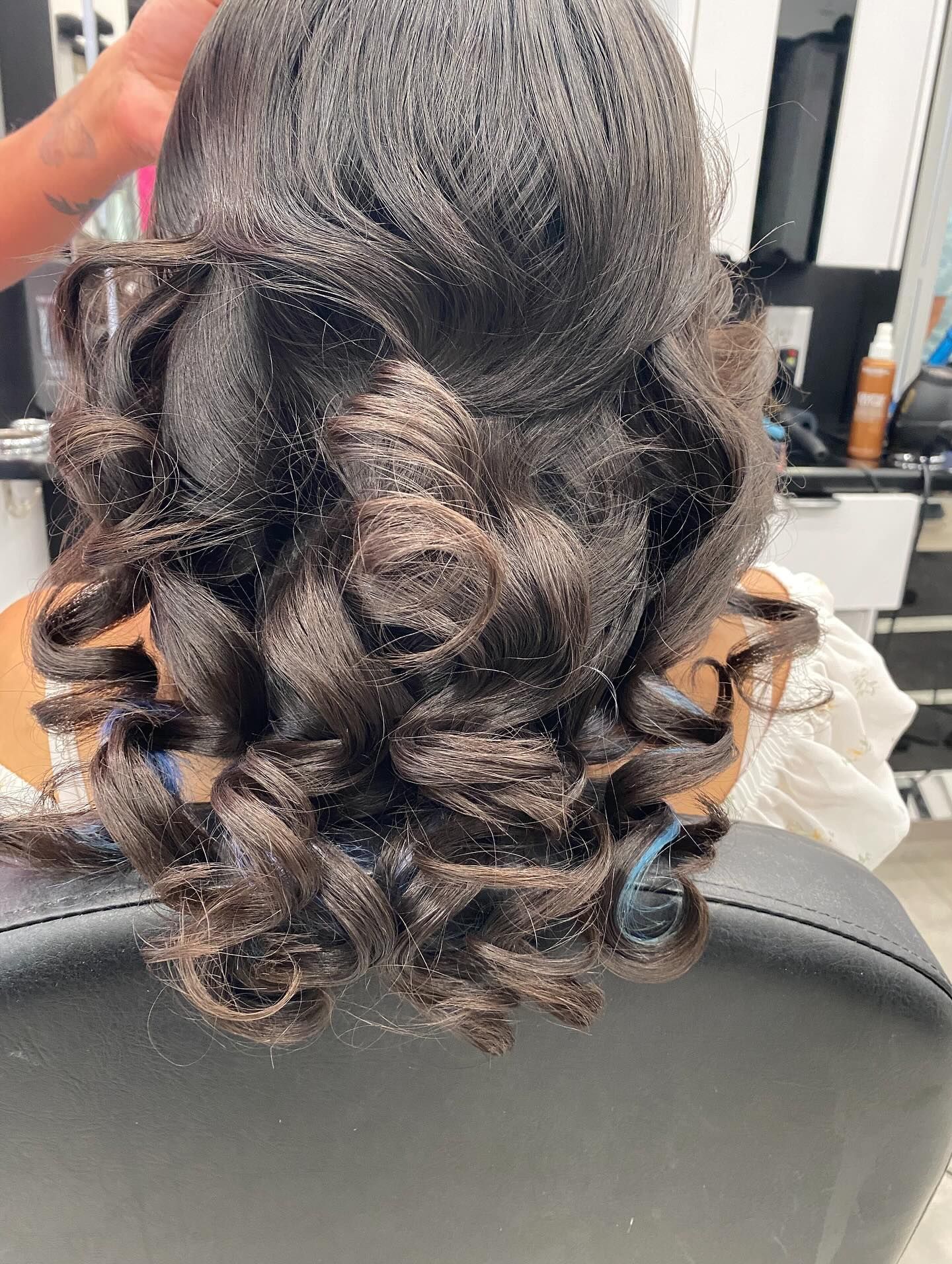 Curly black hair styled half-up with glossy curls, viewed from the back in a salon chair