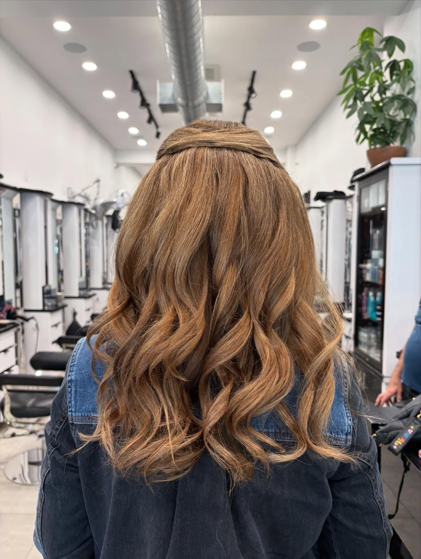 Person with long braided hair seated in a salon, seen from behind.