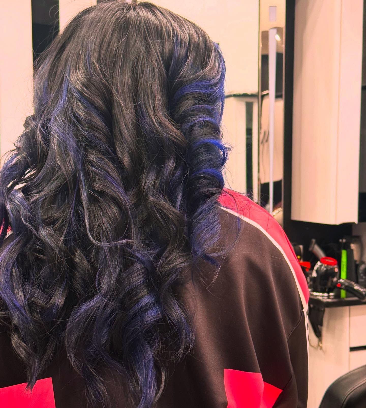 Long wavy dark hair with blue highlights, seen from behind in a salon chair