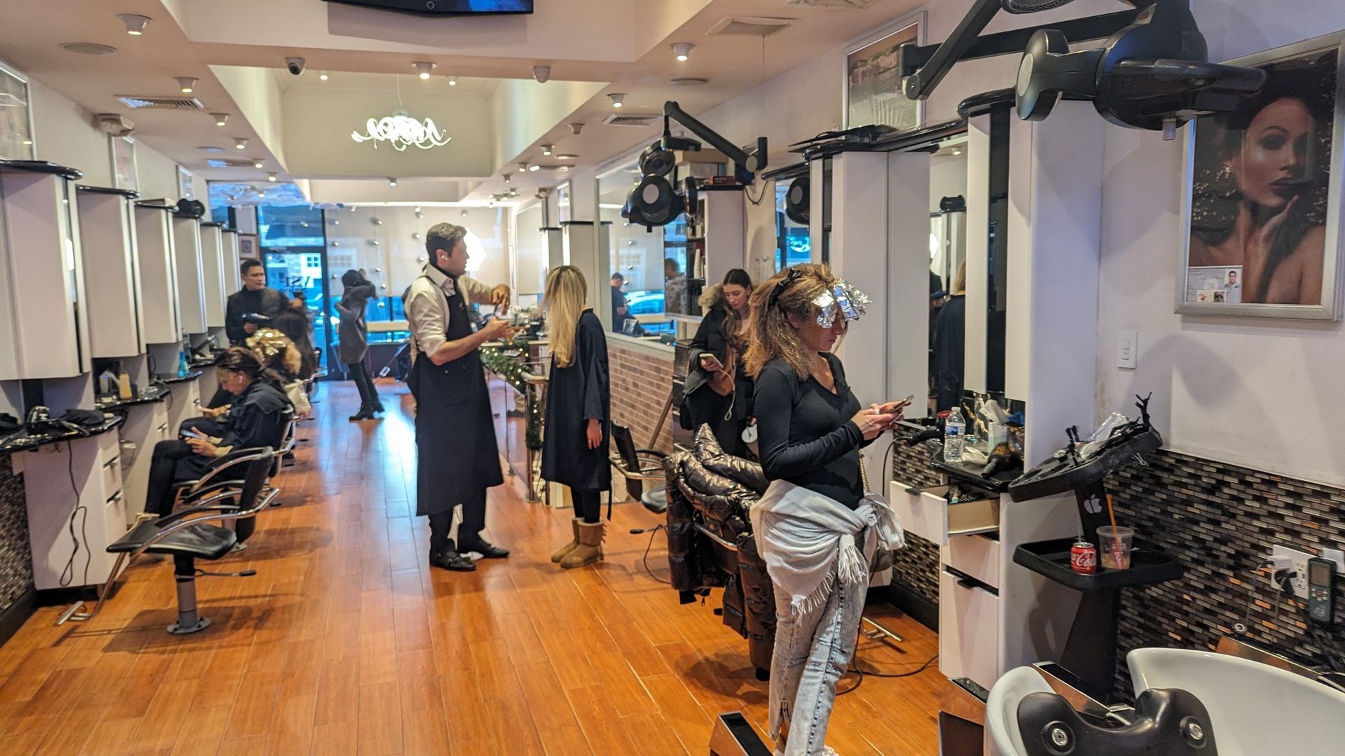 Hair salon interior with stylists working on clients amid mirrors, chairs, and products on wood floors