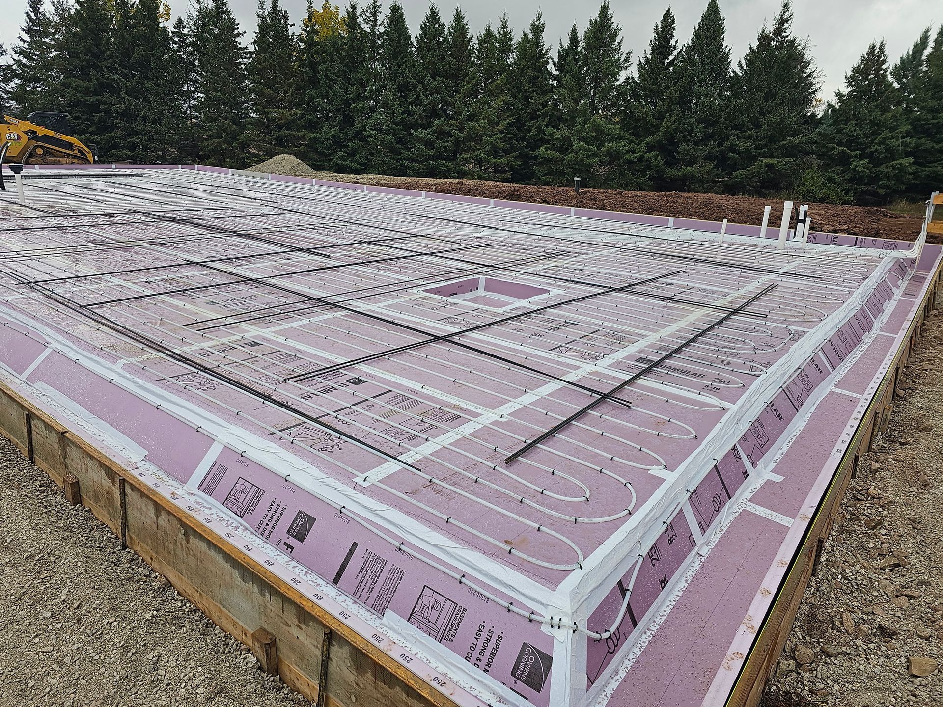 A concrete foundation for a house is being built in a field with trees in the background.