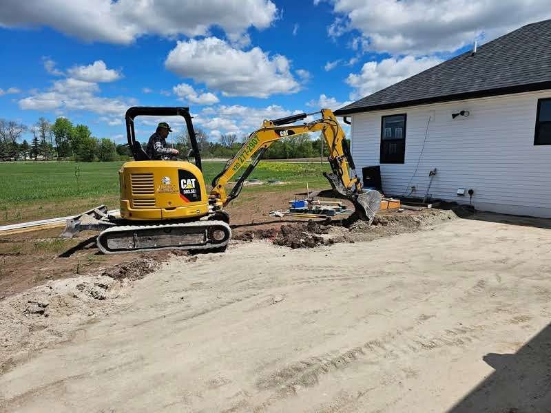 A yellow excavator is digging a hole in the dirt in front of a house.
