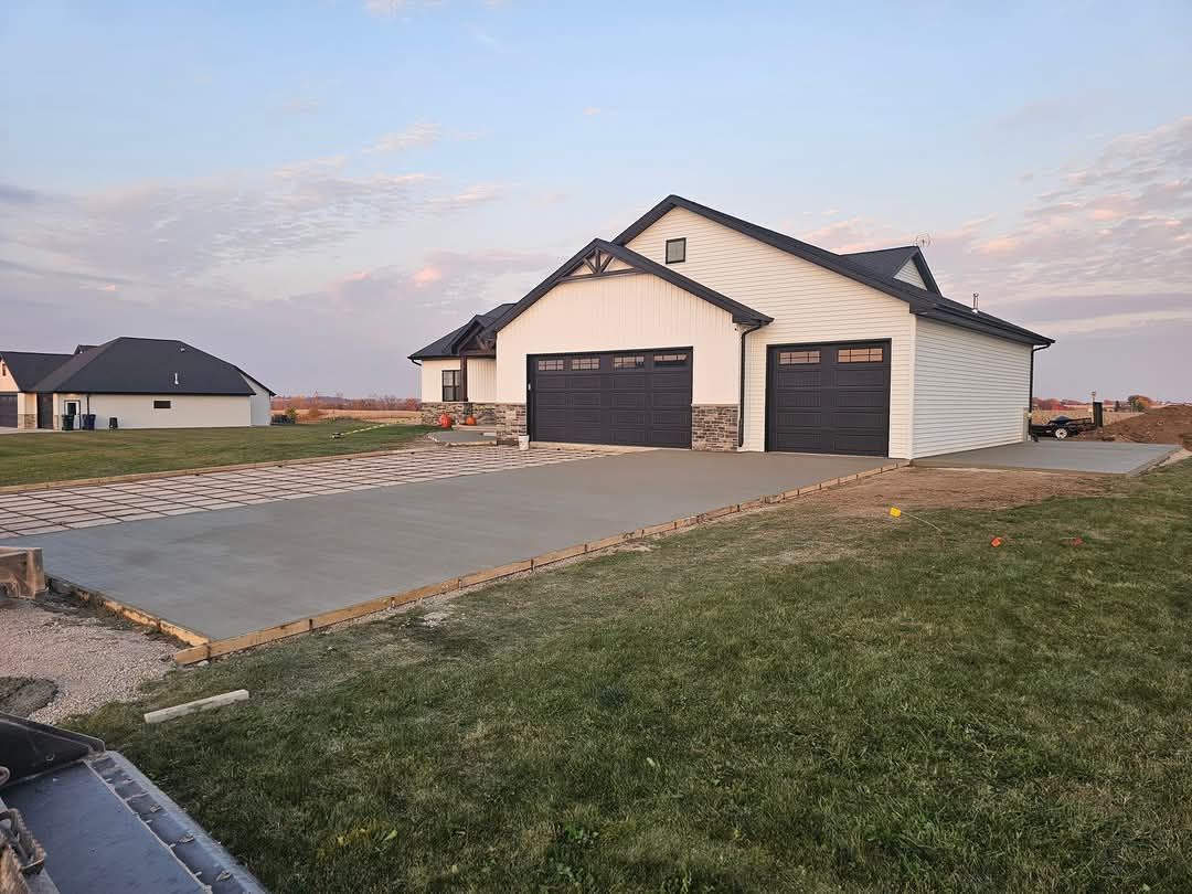 A white house with black garage doors and a concrete driveway in front of it.
