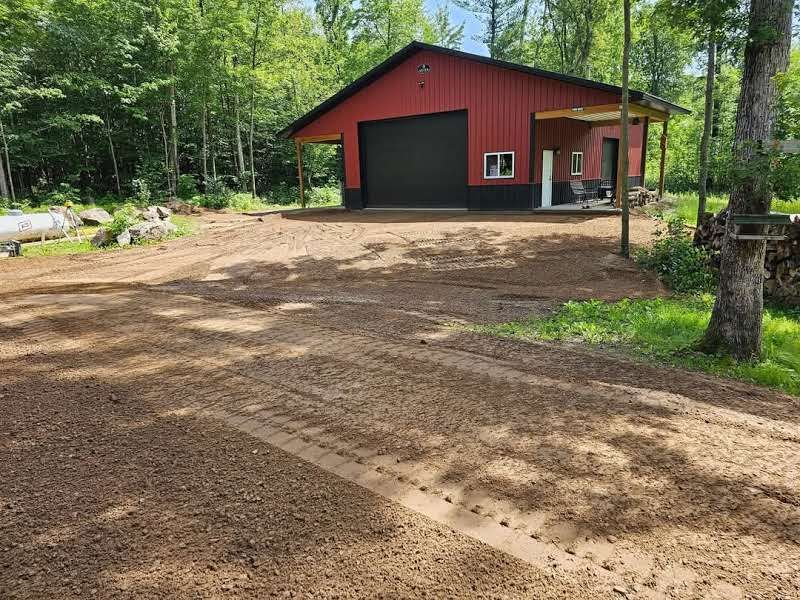 A red garage with a black door is in the middle of a dirt road.