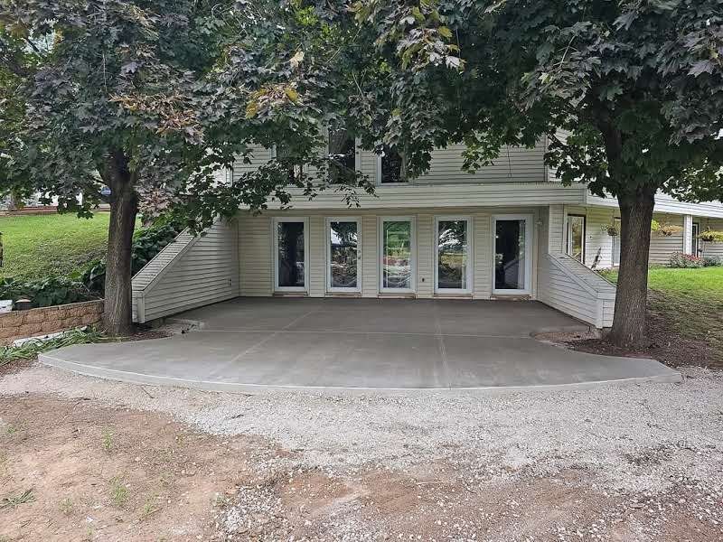 A house with a concrete driveway underneath it and trees in front of it.