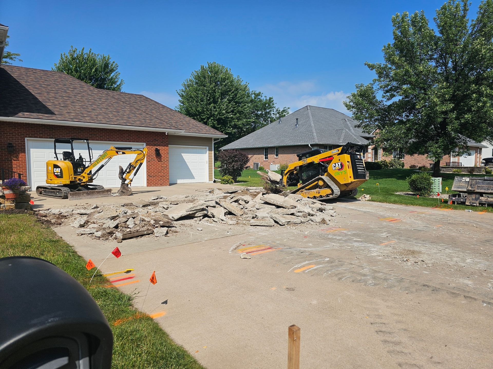 A yellow excavator is sitting in a driveway next to a house.