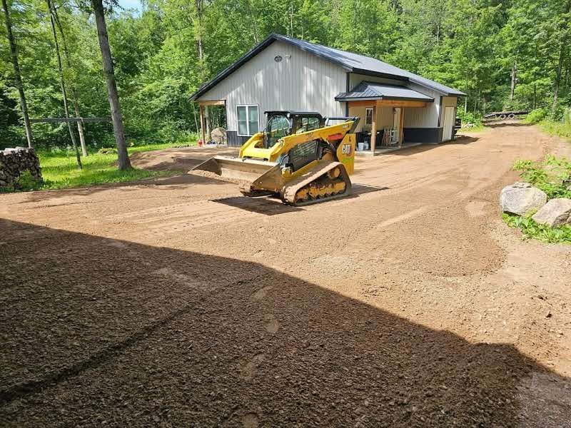 A bulldozer is driving down a dirt road in front of a house.