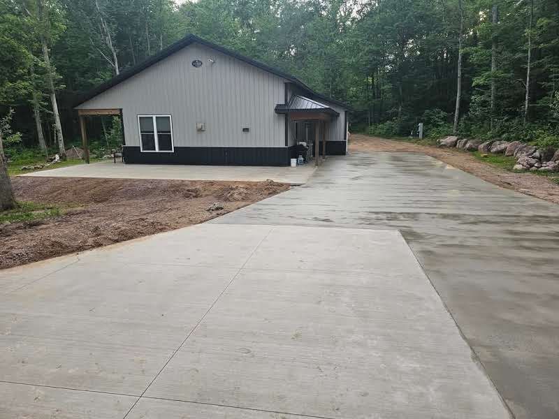A house with a concrete driveway leading to it is surrounded by trees.