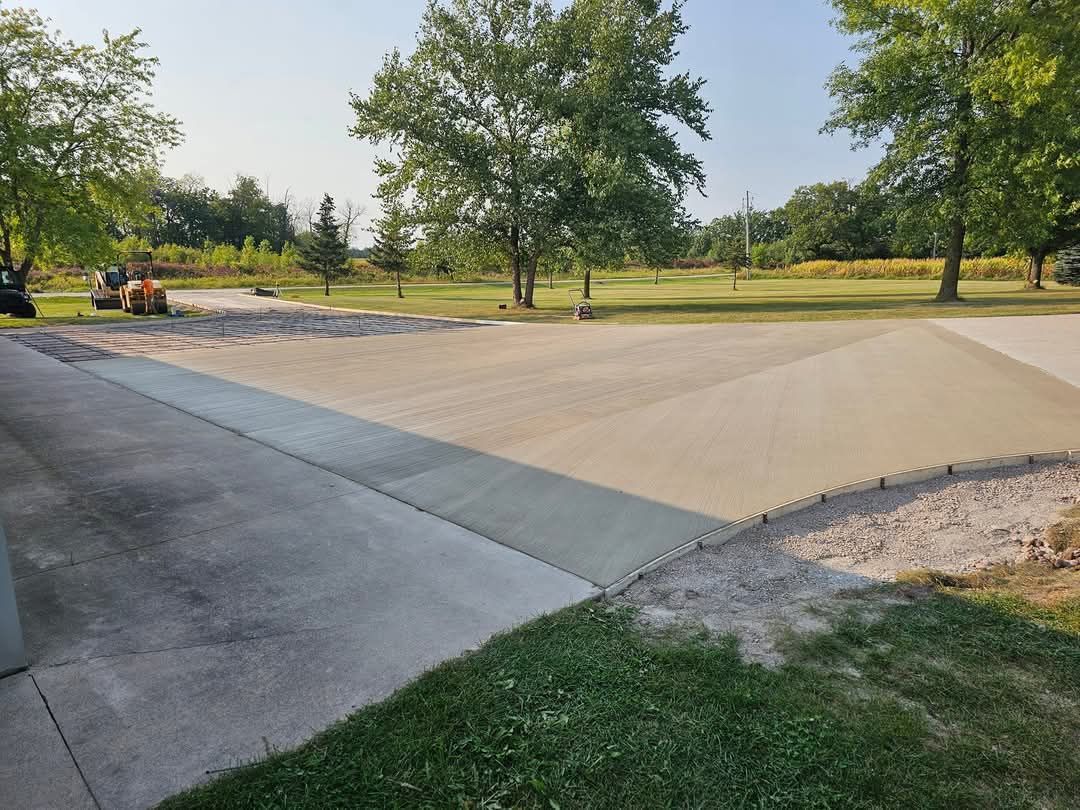 A concrete driveway leading to a park with trees in the background.