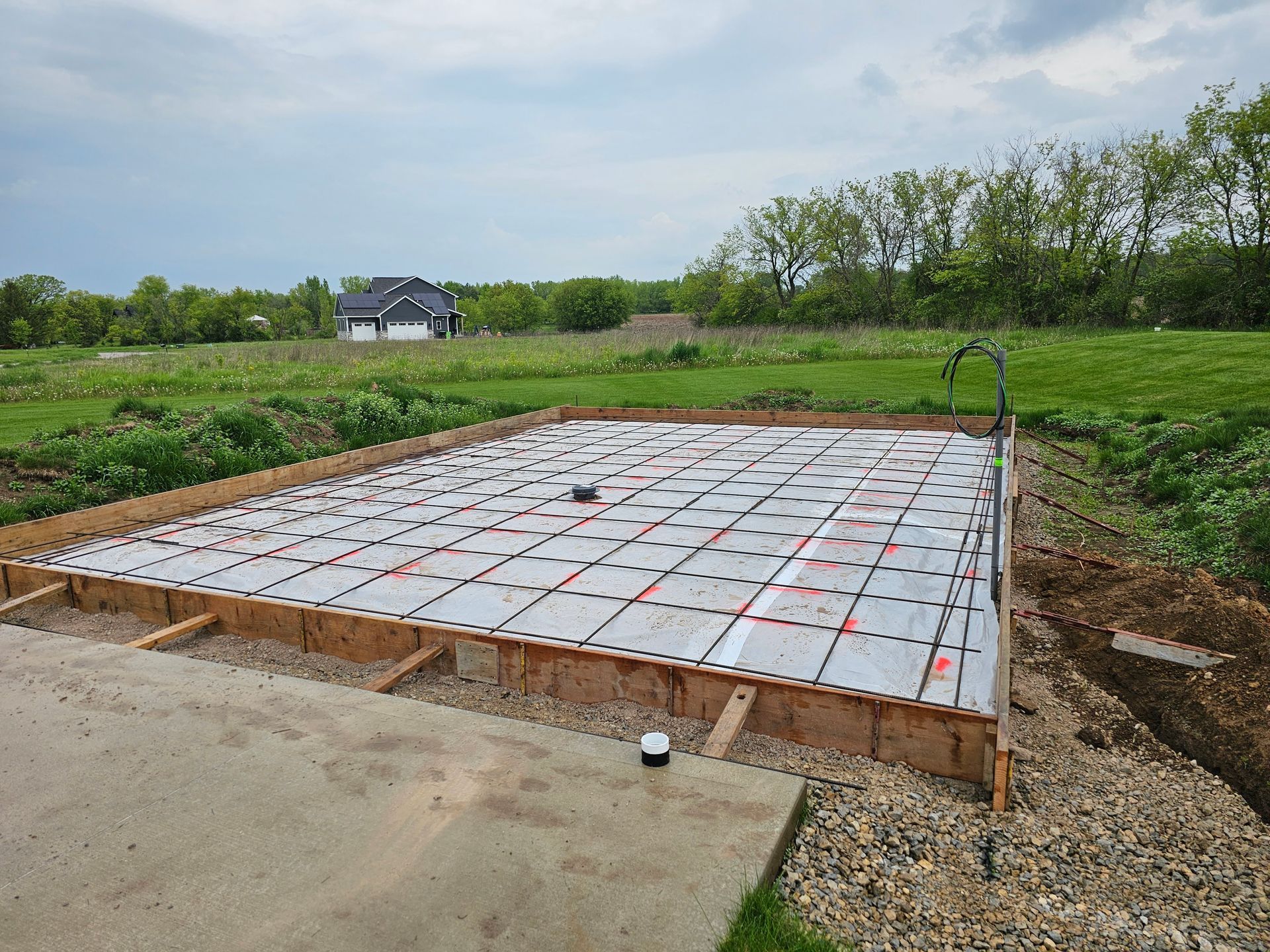 A concrete foundation is being built in a field with a house in the background.