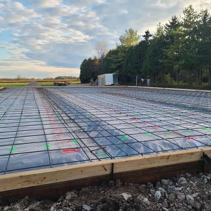 A concrete foundation is being built in a field with trees in the background.