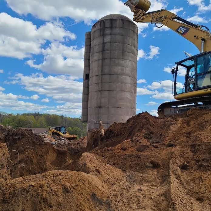 A bulldozer is digging a hole in front of a silo.