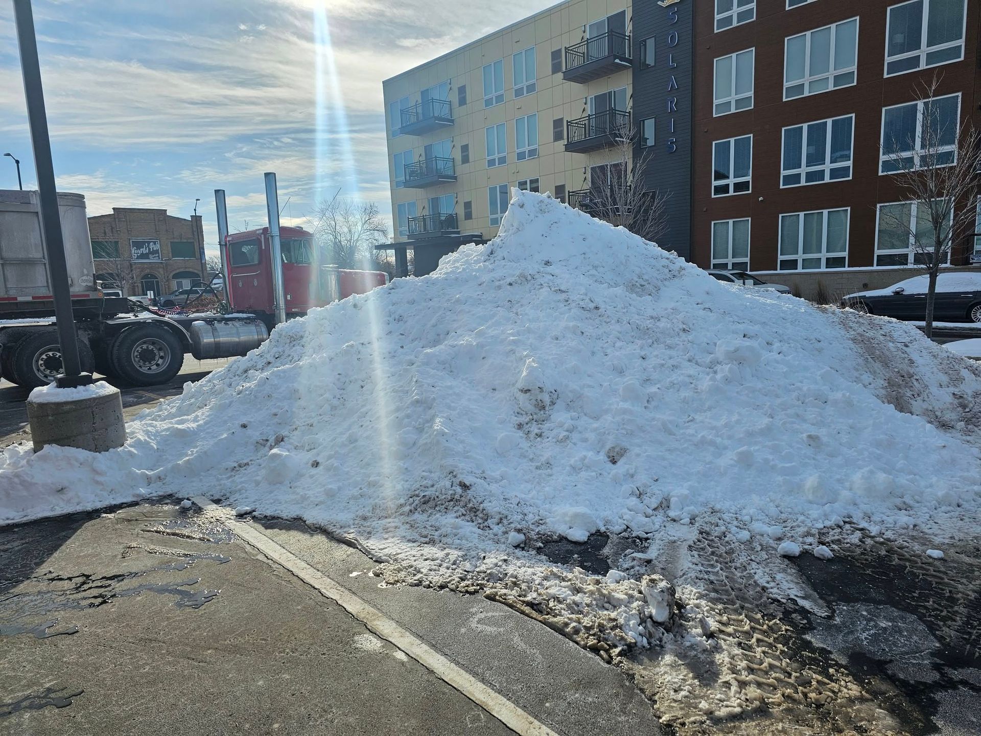 A large pile of snow is sitting on the side of the road in front of a building.