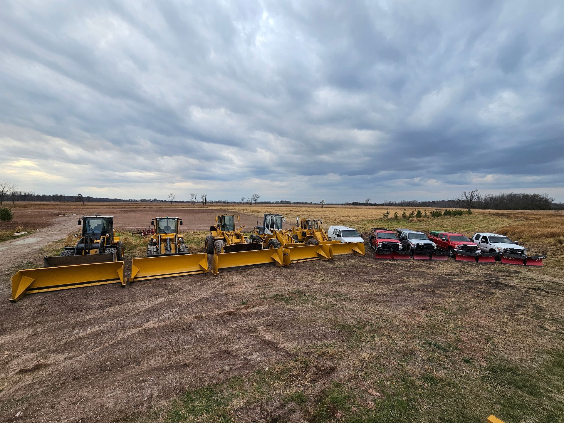 A row of tractors and trucks are parked in a field.