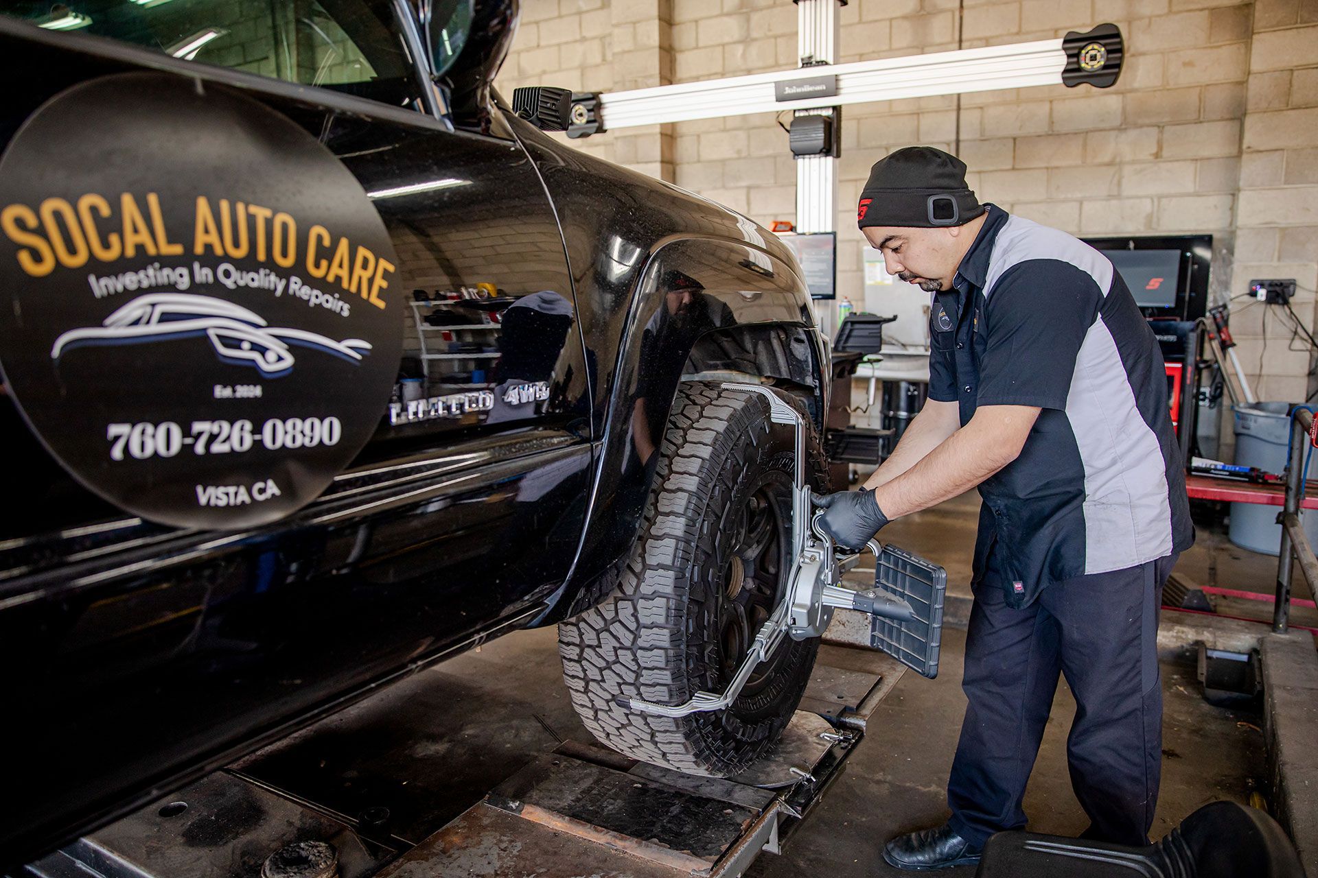 Mechanic rotating a truck tire in an auto shop beside a black SoCal Auto Care vehicle