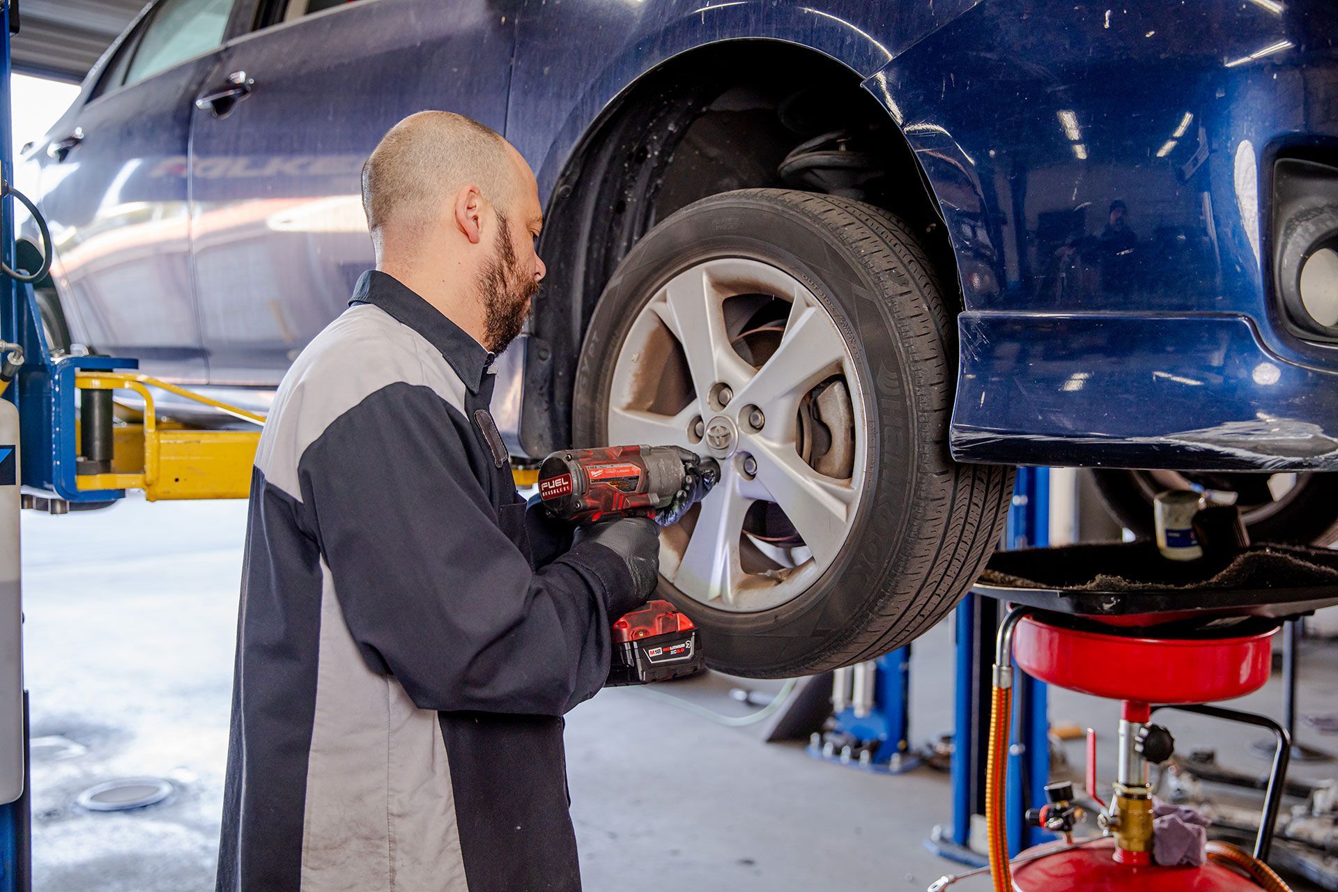 Mechanic inspecting a blue car’s wheel on a lift in an auto repair shop
