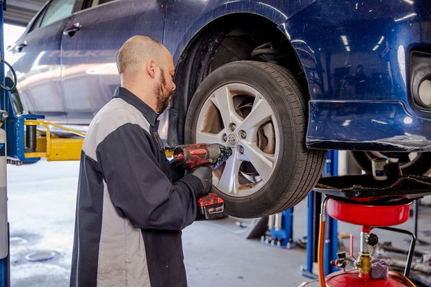 Mechanic inspecting a blue car’s wheel on a lift in an auto repair shop