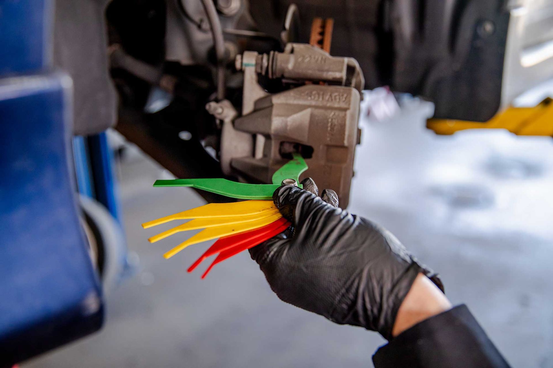 Gloved mechanic handling colored brake pad shims near a car wheel assembly