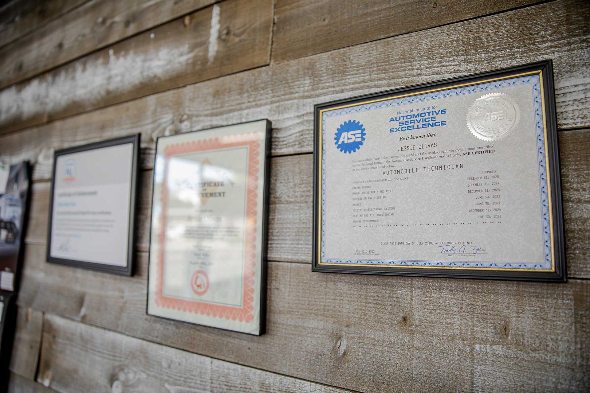 Three framed certificates and notices mounted on a weathered wooden wall.