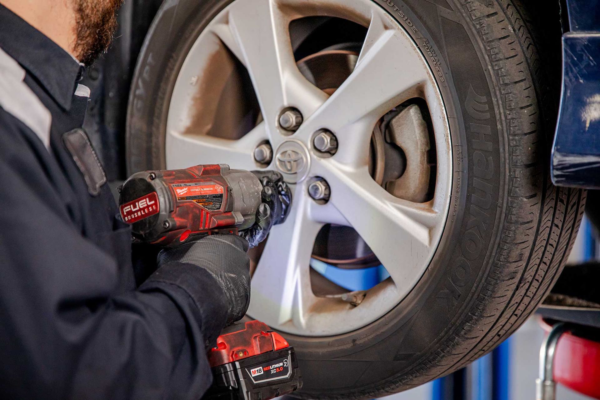 Mechanic using a red impact wrench to tighten a car wheel lug nut