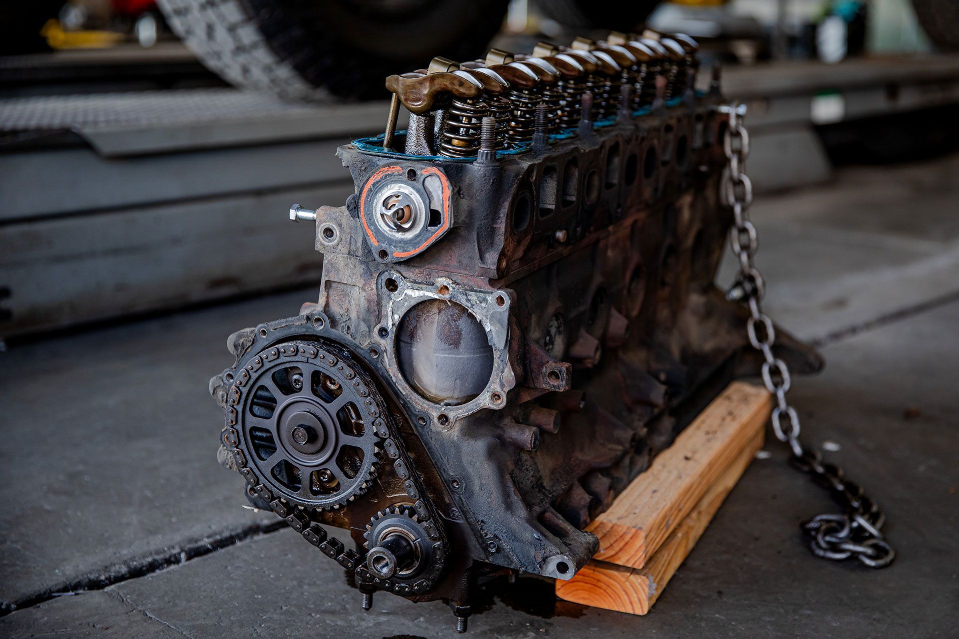 Rusty engine block with exposed gears and chain, resting on wooden blocks in a workshop.
