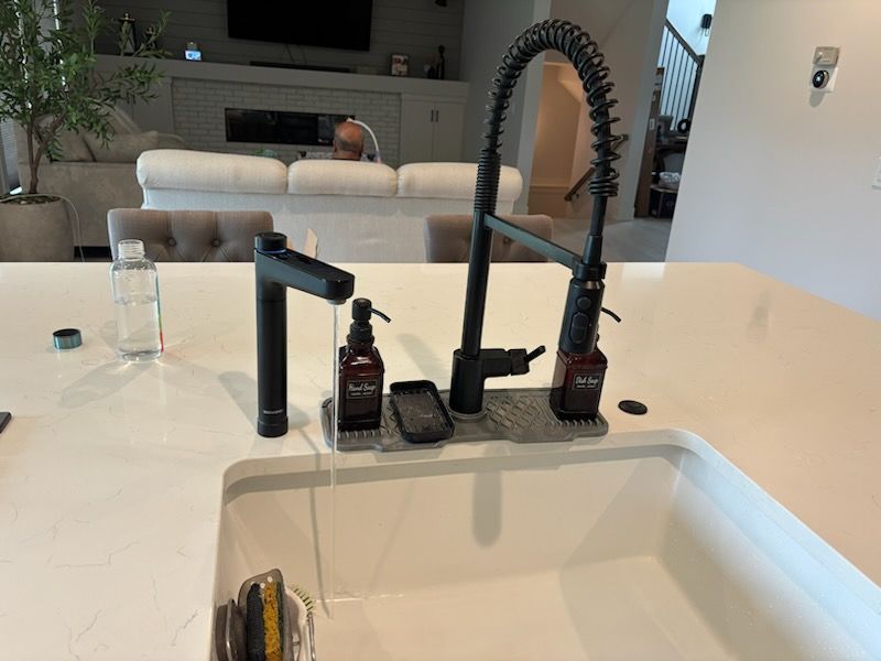 Black kitchen faucet with soap dispensers on a white countertop, water running into a white sink.