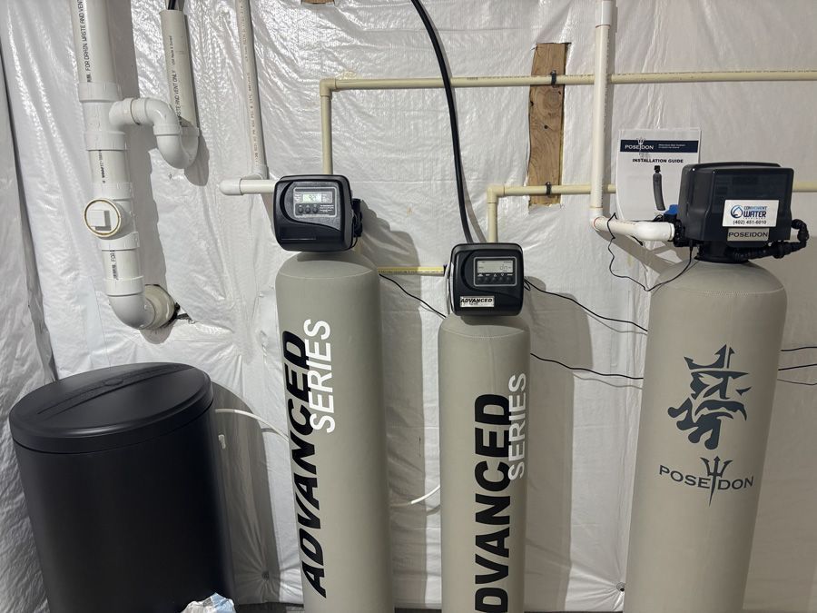 Water filtration system in a basement; three cylindrical tanks, digital displays, and connected piping.