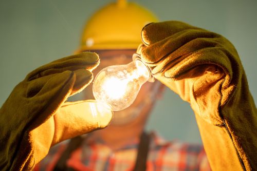 Worker in yellow gloves replacing a glowing light bulb under a hard hat