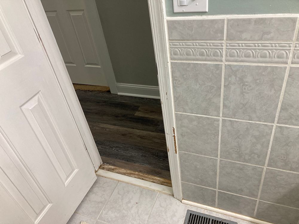 A bathroom with a tiled wall and a wooden floor.