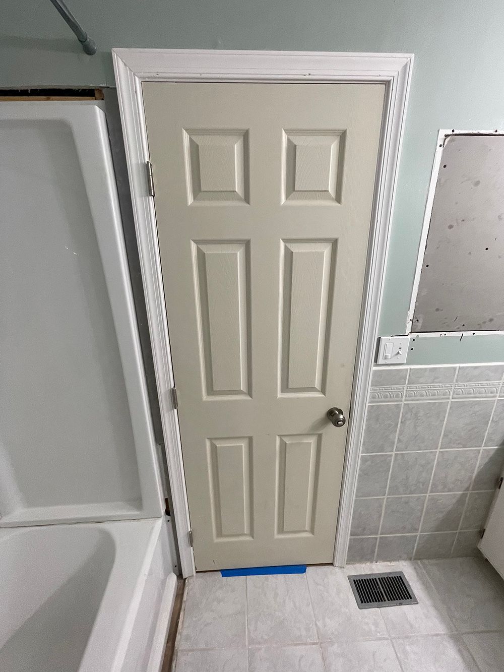 A white door is in a bathroom next to a bathtub.