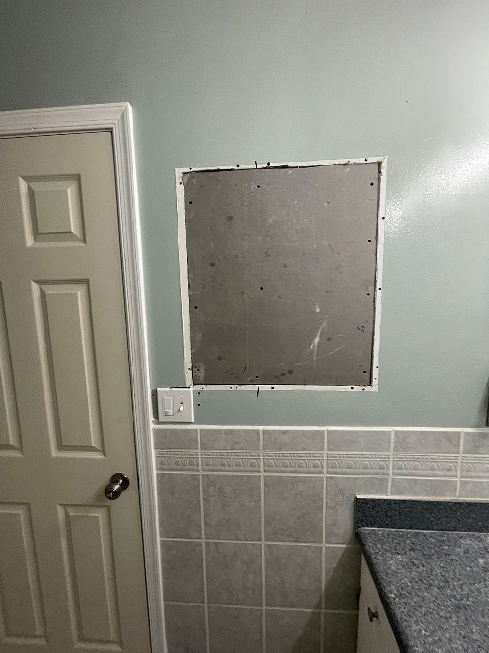 A bathroom with a hole in the wall and a door.