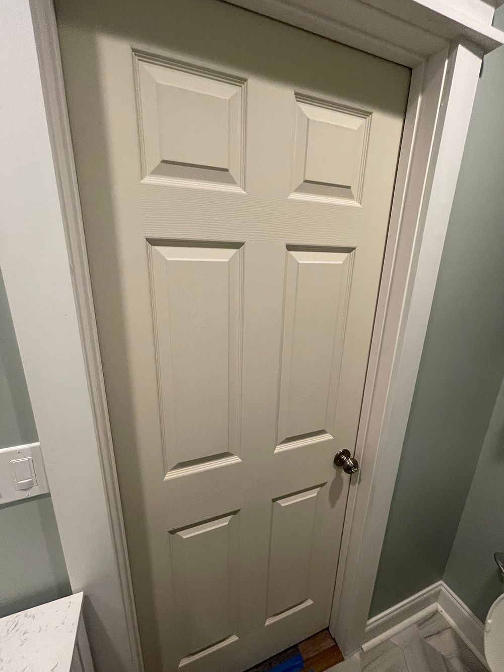 A white door in a bathroom next to a toilet.