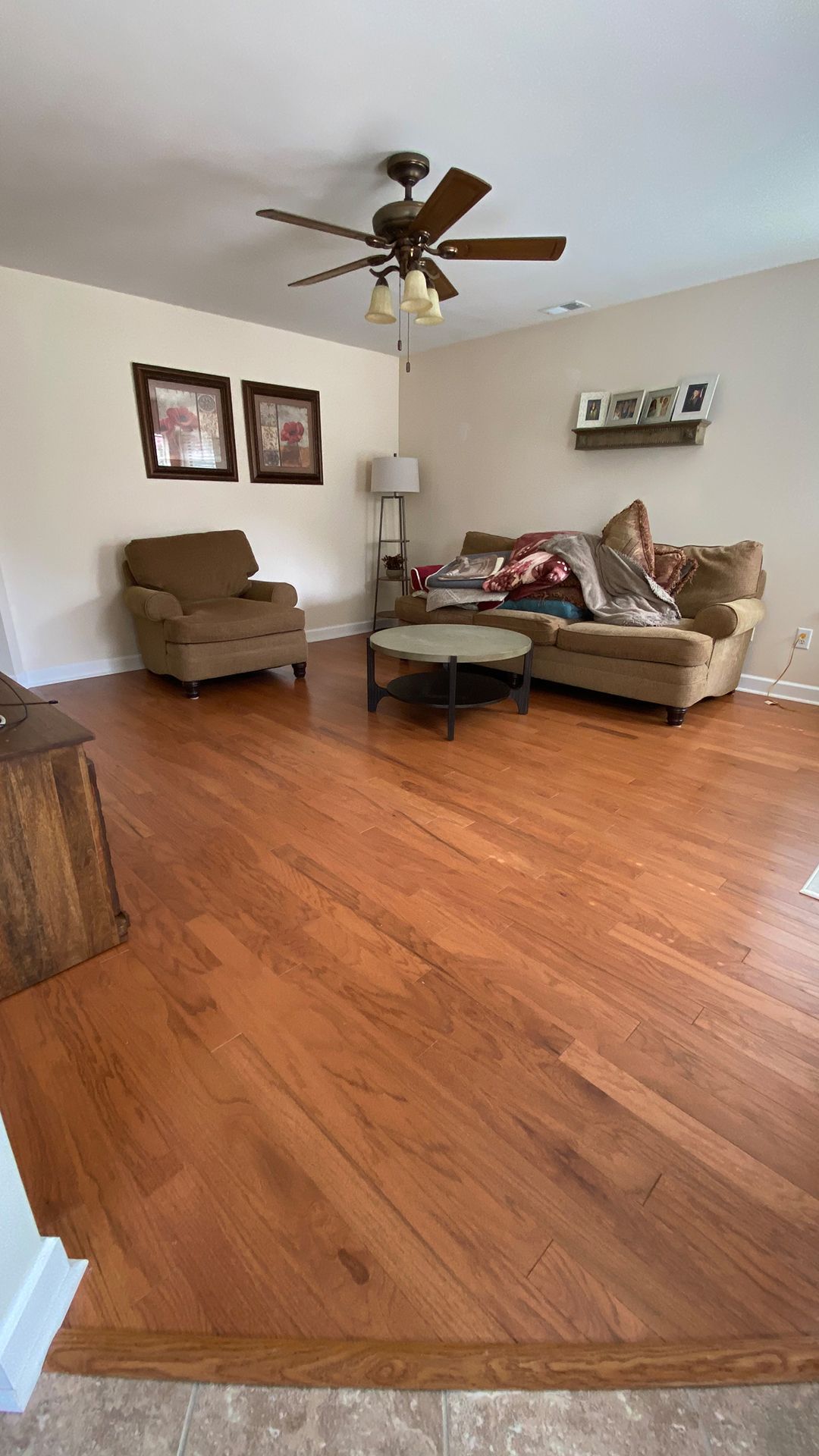 A living room with hardwood floors, a couch, chairs, and a ceiling fan.